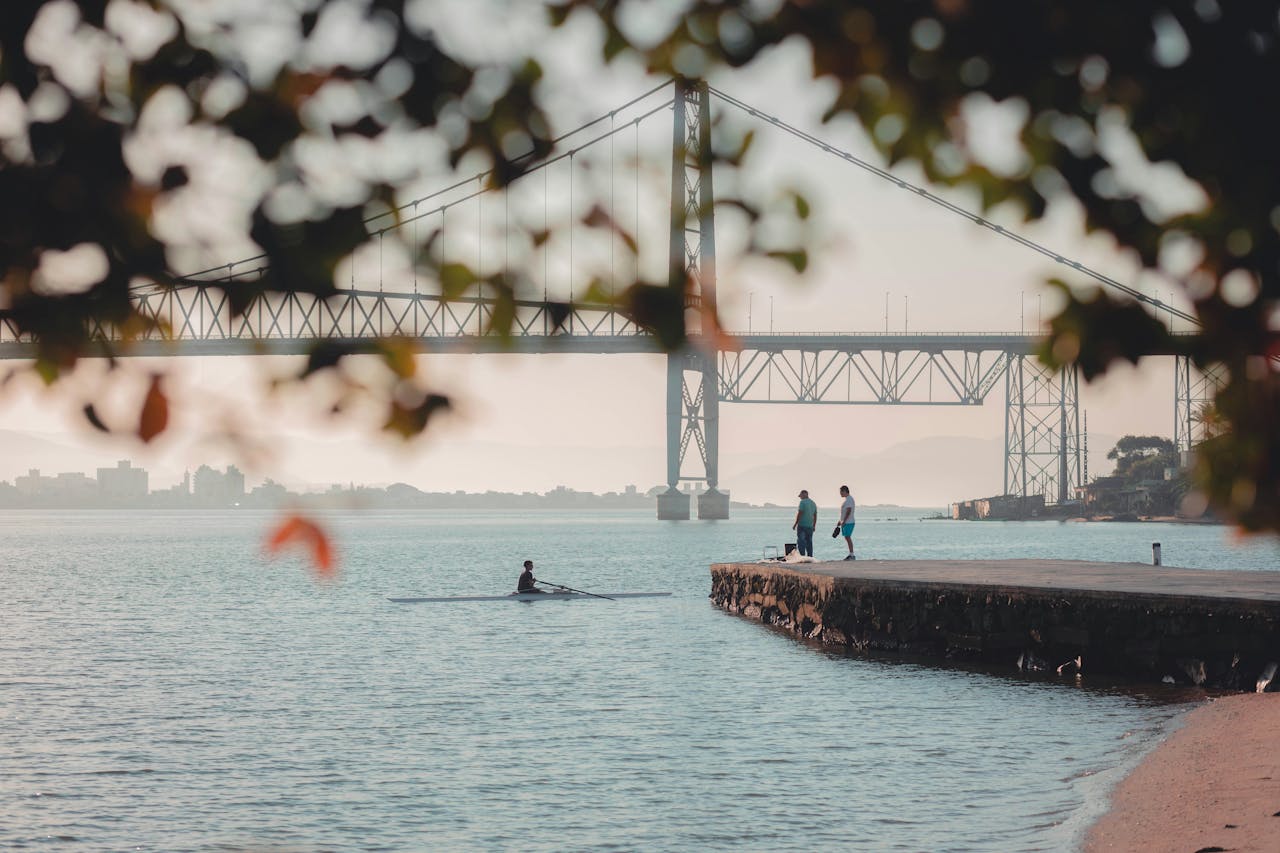 Serene scene at Florianópolis pier with rowing and bridge view.